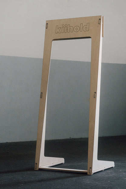 Freestanding wooden hanger with 'Kiihold' branding on a gray floor against a gray wall

