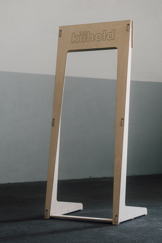 Freestanding wooden hanger with 'Kiihold' branding on a gray floor against a gray wall

