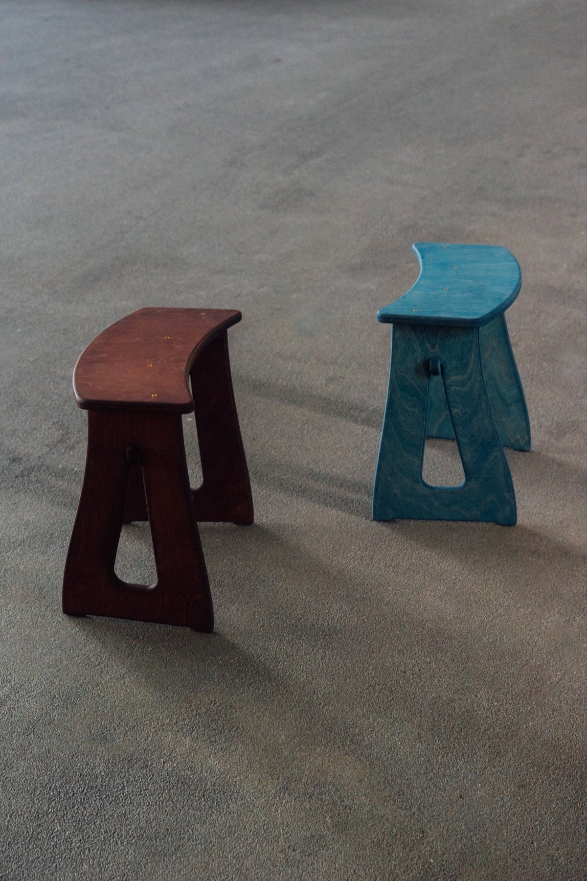 Two stools, one brown and one blue, on a textured gray surface.